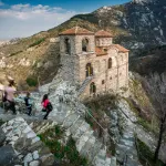 Medieval church of Asen's Fortress on a rocky ridge with visitors on the stone path