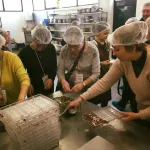 Travellers in hairnets making chocolates together in a workshop