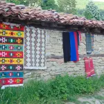 Colourful woven rugs drying on the wall of a stone house
