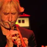 A trumpet player performing on stage under warm lights